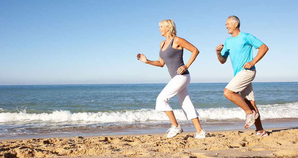 Senior Couple In Fitness Clothing Running Along Beach