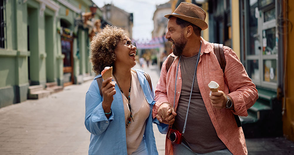 Cheerful couple of tourists laughing and eating ice cream while walking on their trip.