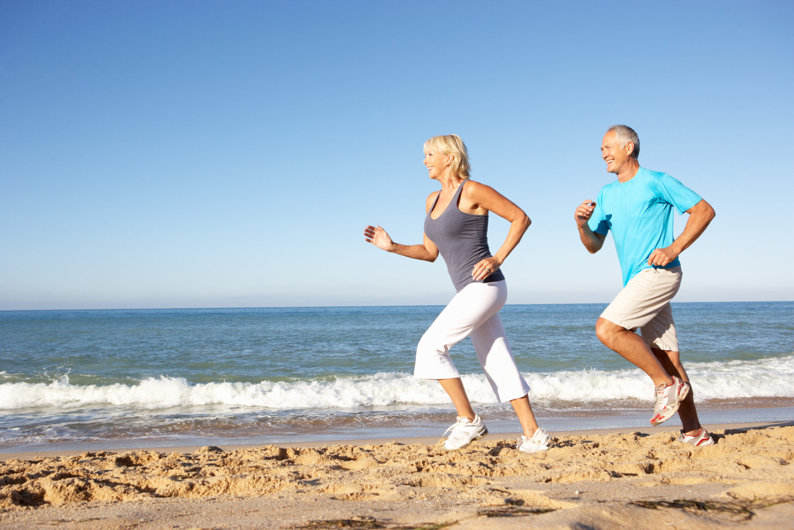 Senior,Couple,In,Fitness,Clothing,Running,Along,Beach